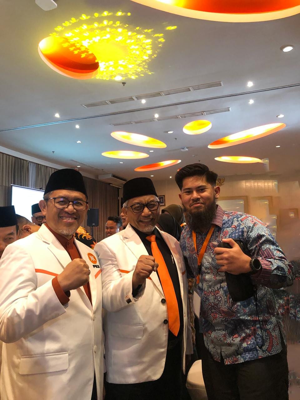 Wira in a batik shirt posing with two men in white PKS jackets at a PKS party event